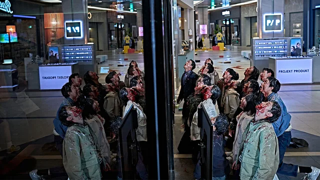 Un grupo de infectados con ropa ensangrentada mira hacia arriba dentro de un centro comercial.