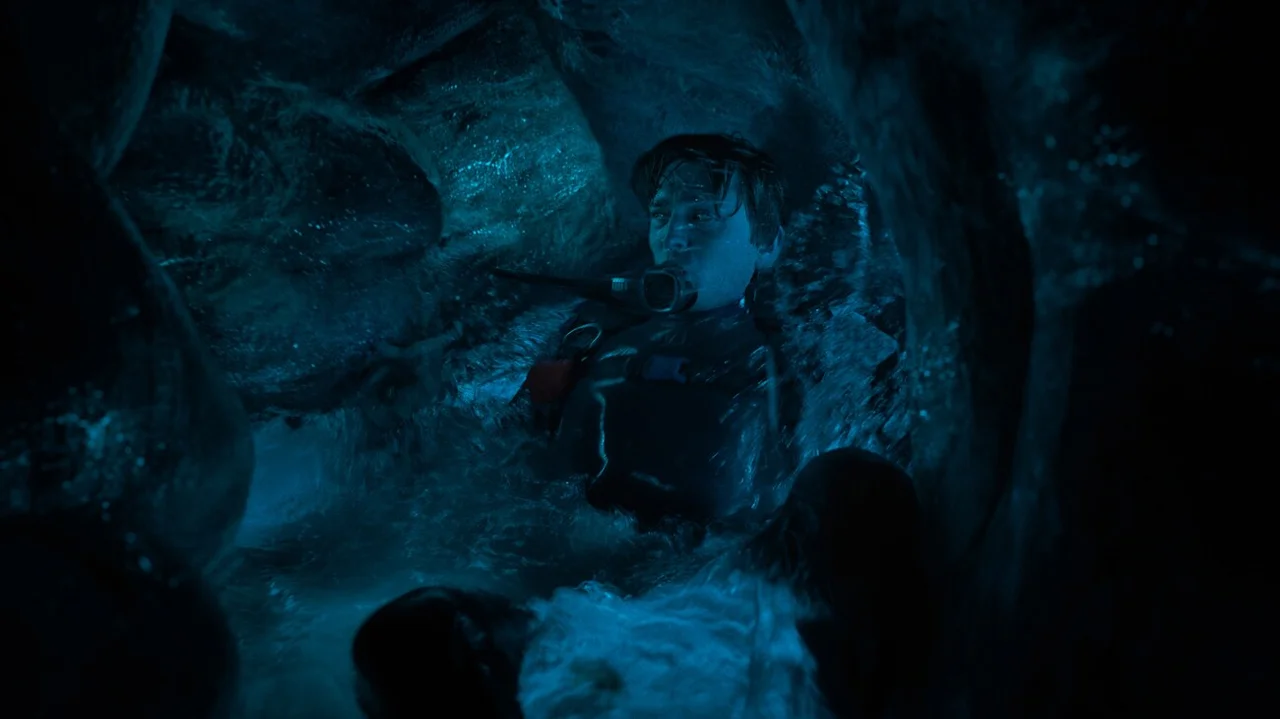 Austin Abrams con equipo de buceo en un espacio oscuro de paredes orgánicas, en La caída de la ballena.