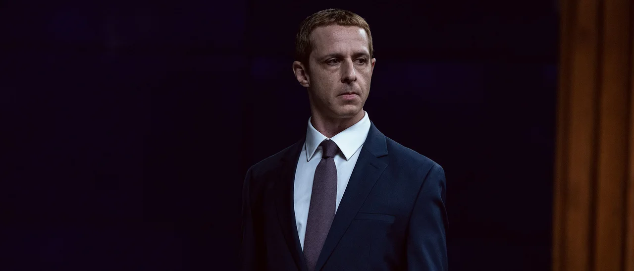 Jeremy Strong, con traje y corbata, mira hacia un costado en El poder de la red.