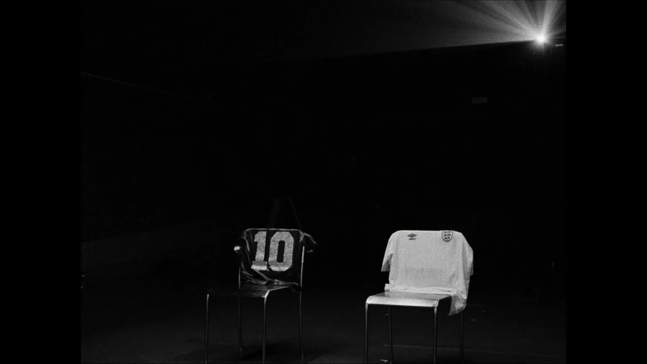 Dos camisetas de fútbol descansan sobre sillas en un espacio oscuro; una es celeste y blanca con el número 10 y la otra es blanca.
