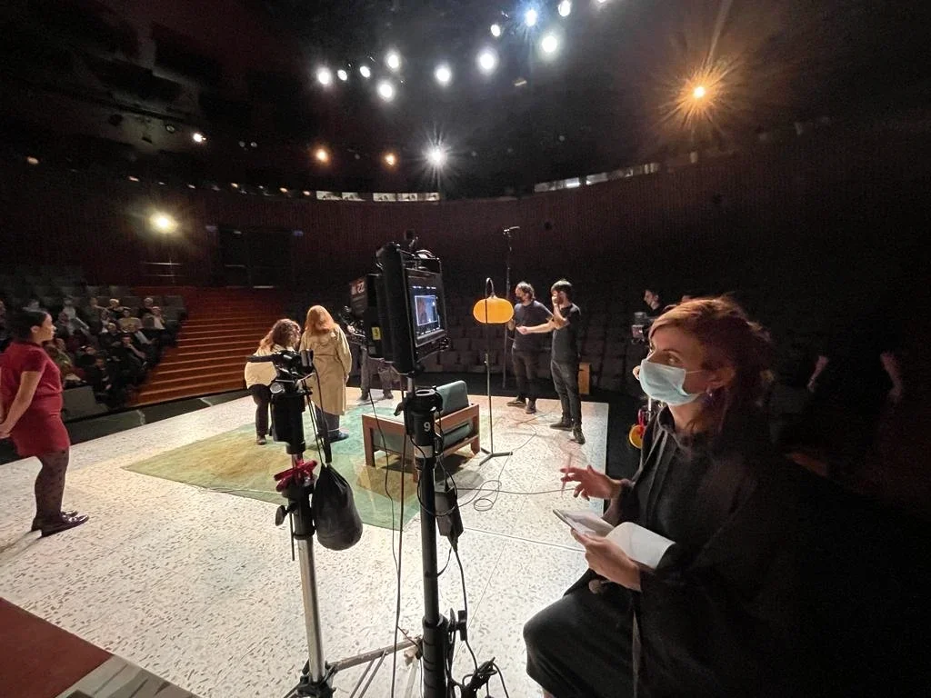 Un equipo trabaja junto a una cámara sobre un escenario frente a las butacas de un teatro.