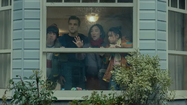 Cuatro integrantes de una familia observan desde una ventana empañada, detrás del vidrio marcado por la lluvia.