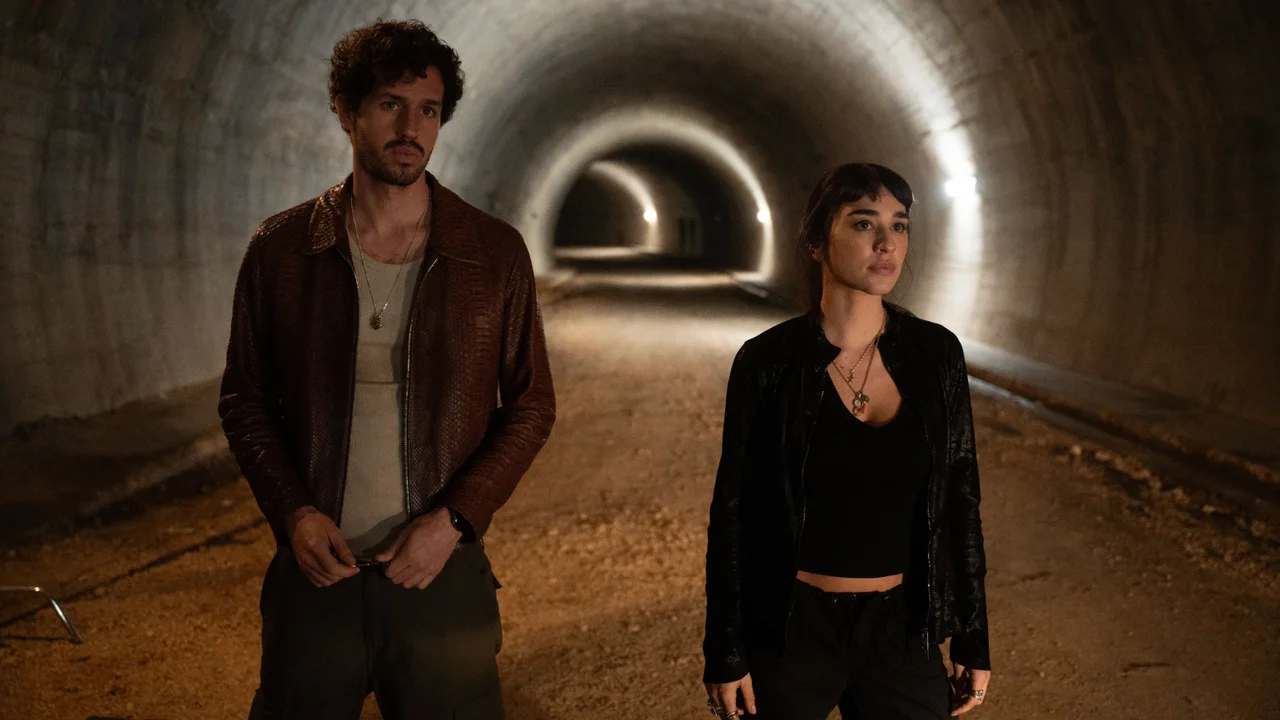 Victor Belmondo y Simona Tabasco están de pie en un túnel de paredes curvas iluminado al fondo.