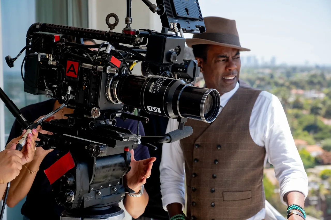 Chris Rock, con sombrero, está junto a una cámara de cine montada para el rodaje.