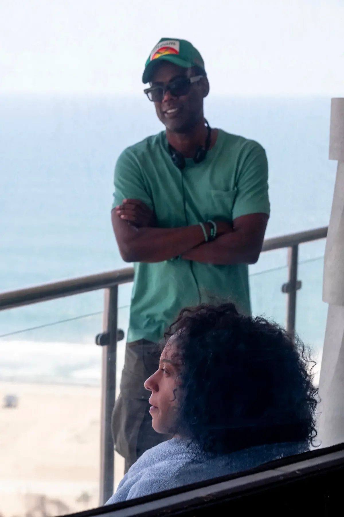 Chris Rock está de pie junto a una baranda mientras Rosalind Eleazar permanece sentada delante de él.