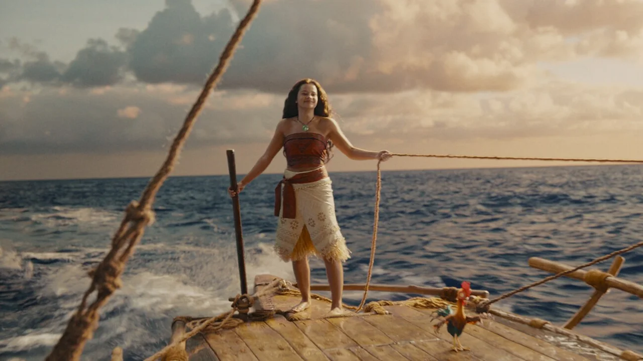 Moana permanece de pie sobre la embarcación mientras navega bajo un cielo iluminado por el sol.