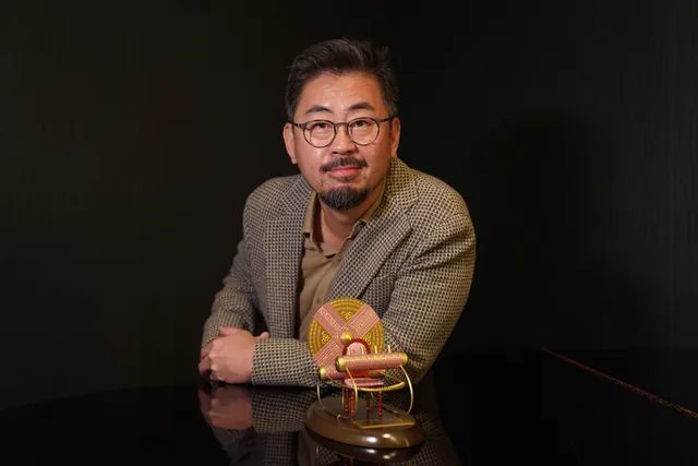Na Hong-jin posa sentado junto al Premio Màquina del Temps, con un fondo oscuro.