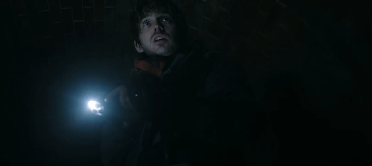 Bryan sostiene una linterna encendida y mira hacia arriba en un lugar oscuro.