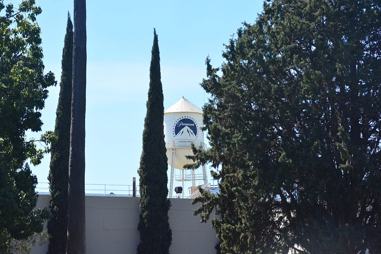 La torre blanca de Paramount Pictures se ve entre árboles altos y sobre los edificios del estudio, bajo el cielo azul.